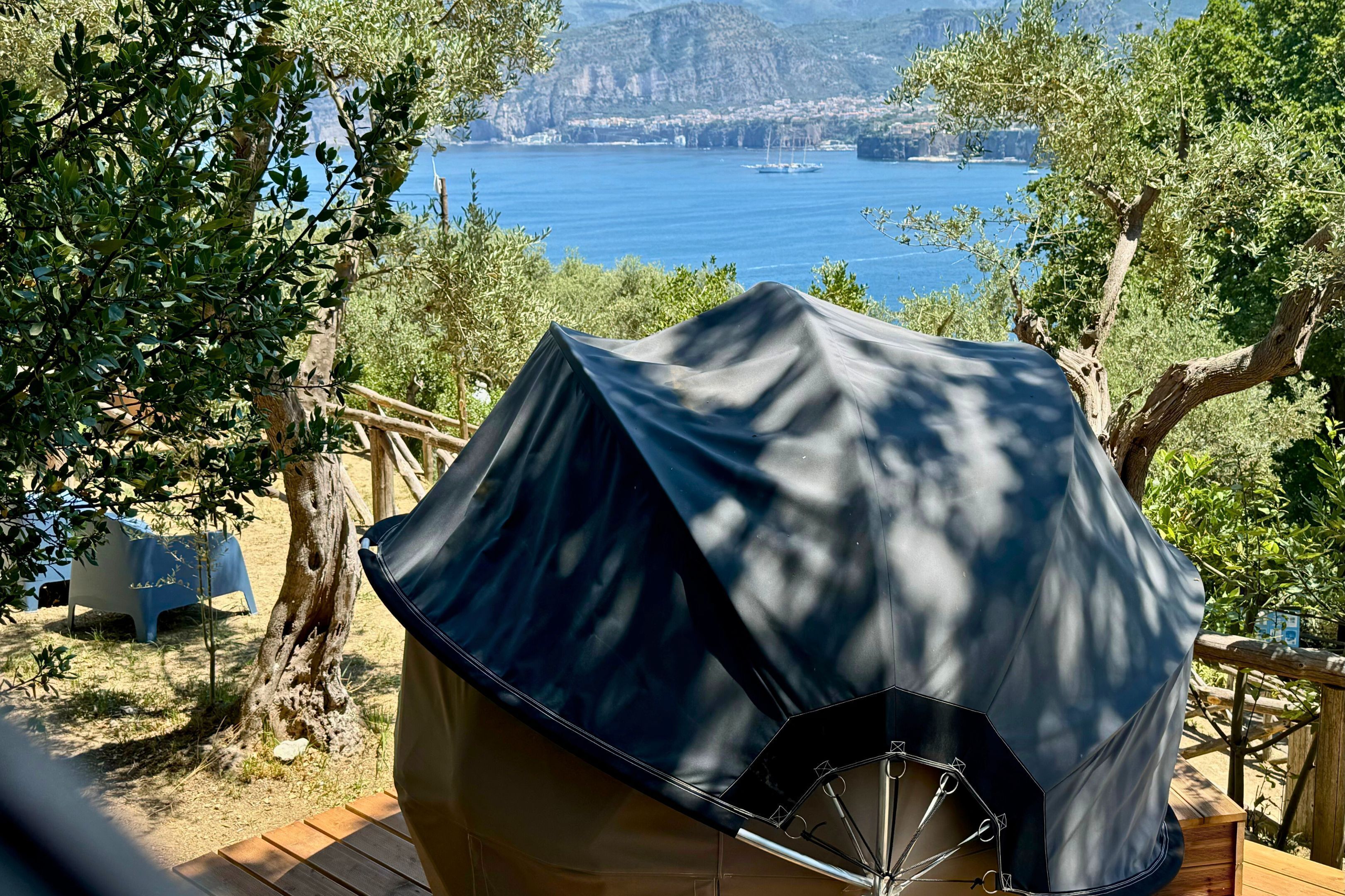 A tent with a black cover, set up on a wooden deck with a view of a body of water and distant landforms.