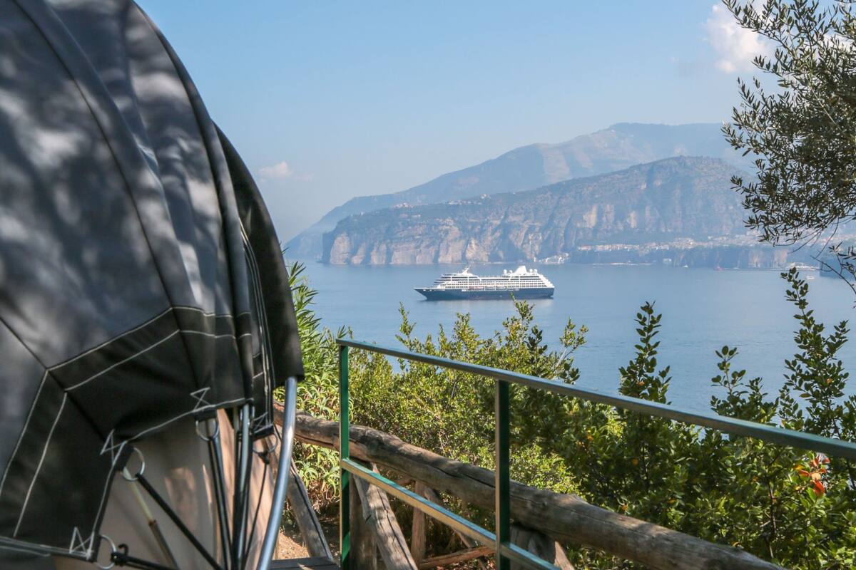 Une vue d’un navire de croisière sur une étendue d’eau calme, avec une côte montagneuse en arrière-plan.