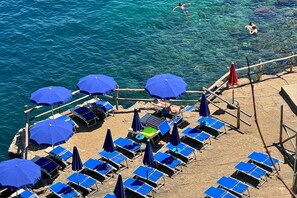 A beach with blue umbrellas, sun loungers, and a wooden walkway. - Hostel & Glamping Santa Fortunata (Sorrento)