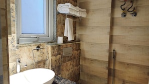 A bathroom with a sink, a towel rack, a shower, and a window.