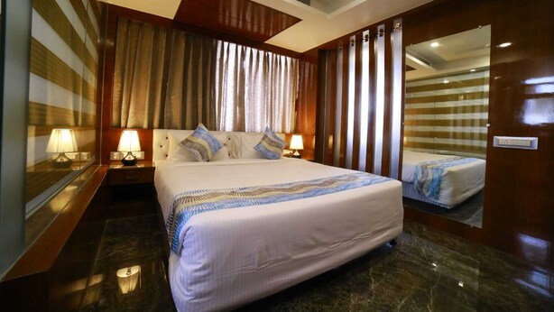 A hotel room with a large bed, two bedside tables with lamps, a mirror, and a view of the room's interior. - GENX JAMUI (Jamui)