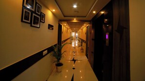 A hotel hallway with framed pictures on the walls, potted plants, and a polished floor. - GENX JAMUI (Jamui)