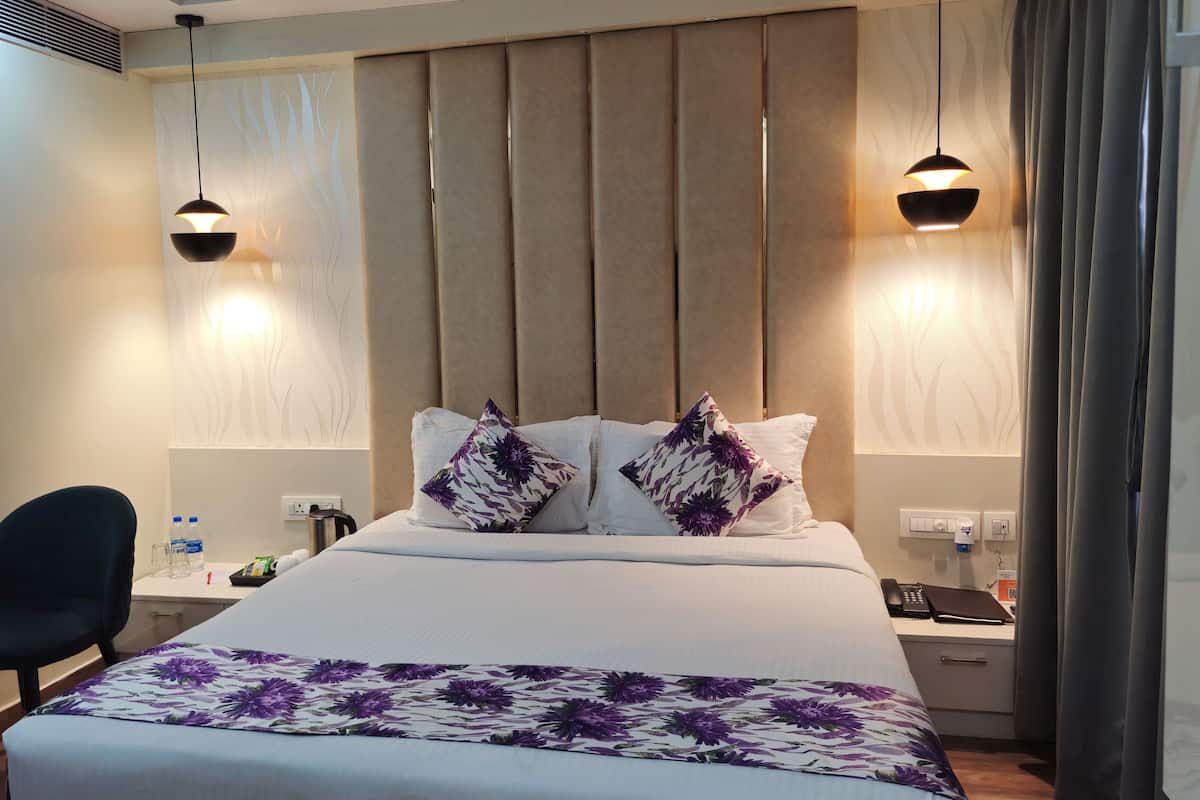 A hotel room with a bed, two bedside lamps, a desk with a phone, and a chair.