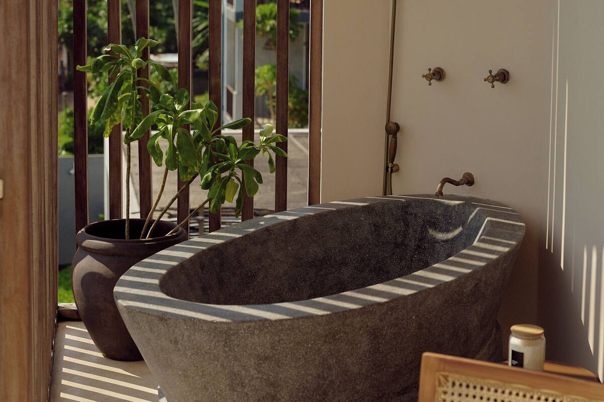 A stone bathtub in a room with a view of palm trees and a balcony.