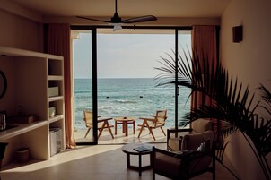 Quarto com vista para o oceano, ventilador de teto, estante de livros e área de estar com cadeiras e mesa.