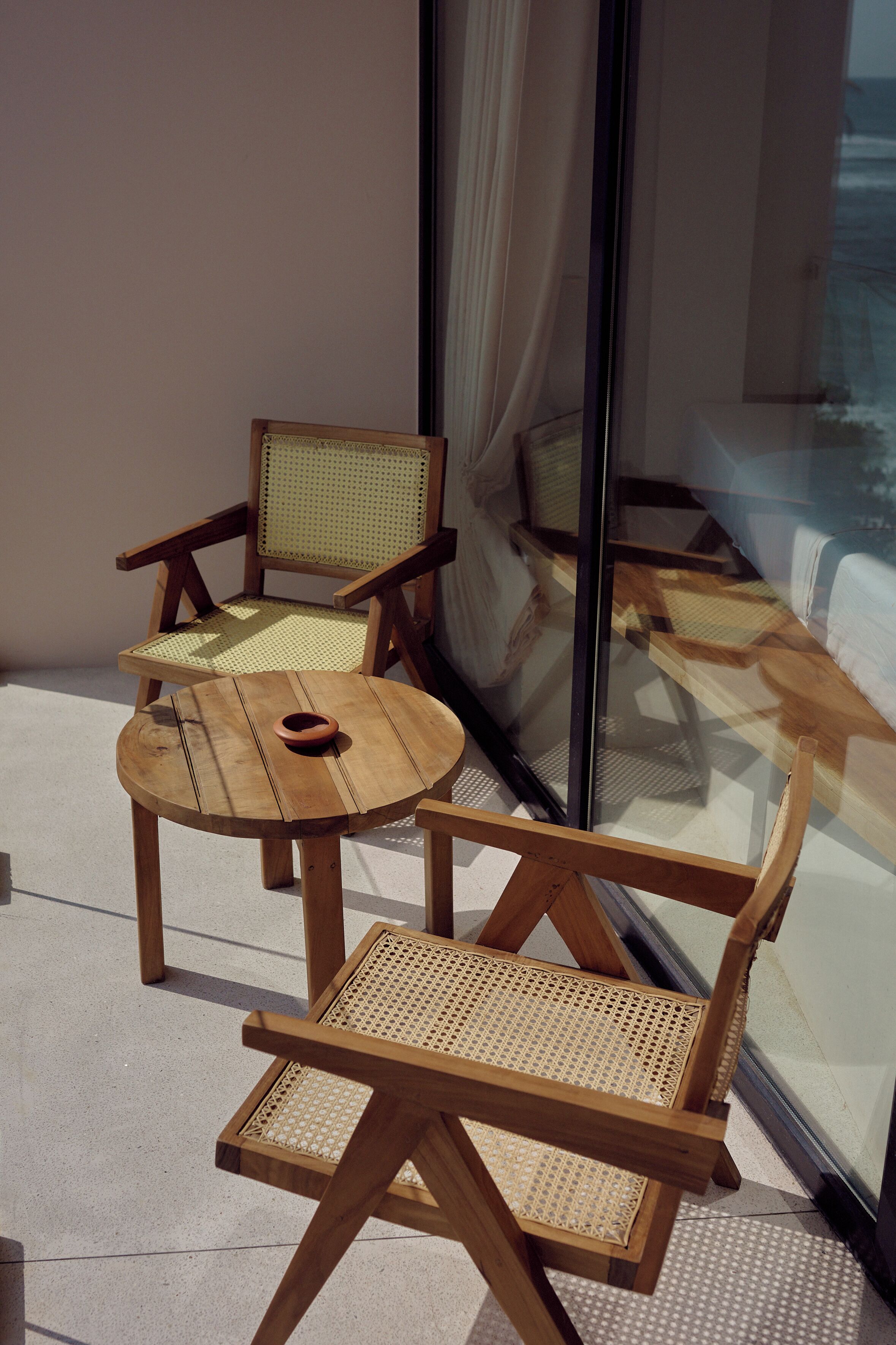 A wooden table and chairs with woven seats, positioned near a glass window.