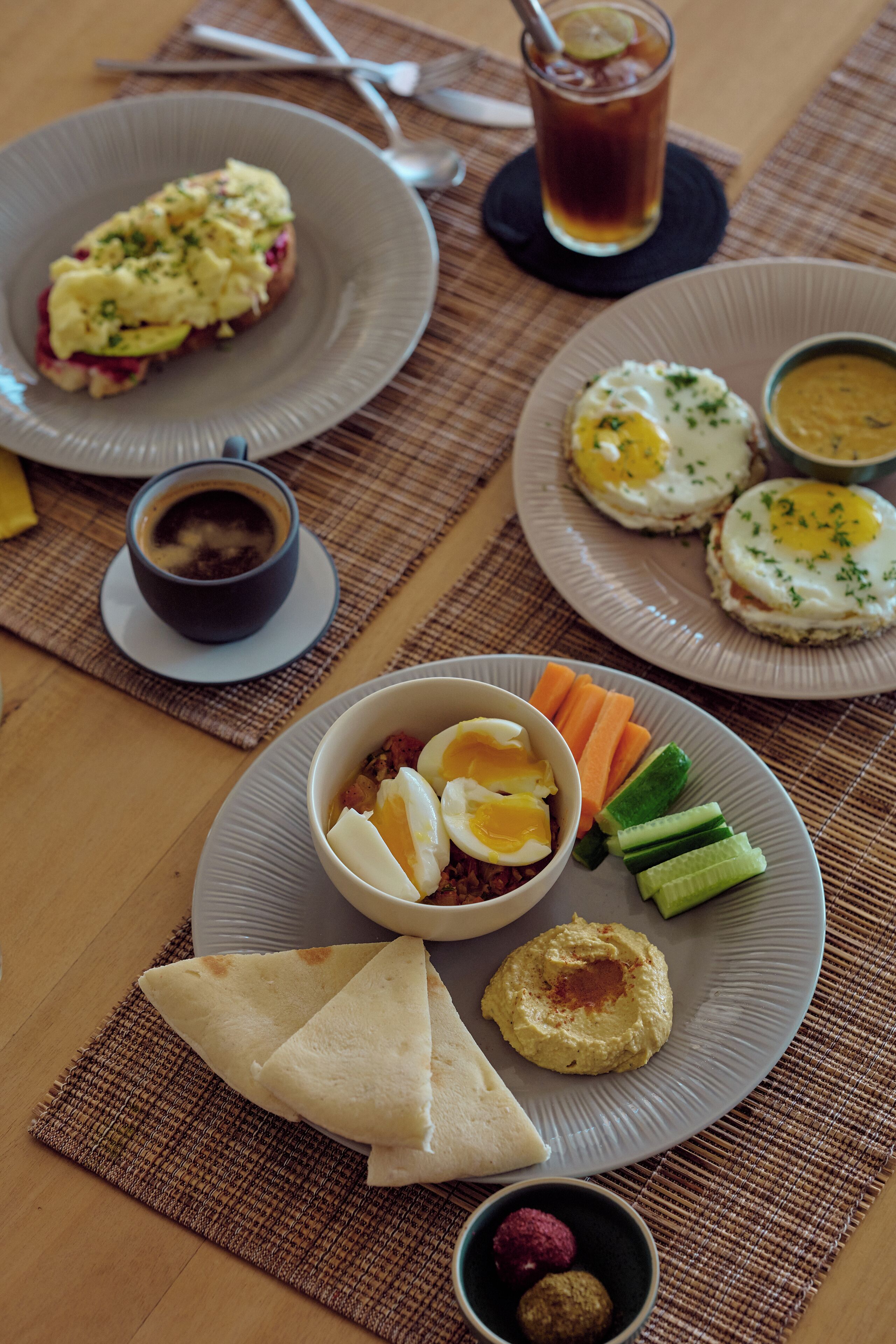 A table with plates of food, including eggs, vegetables, and hummus, along with a cup of tea.