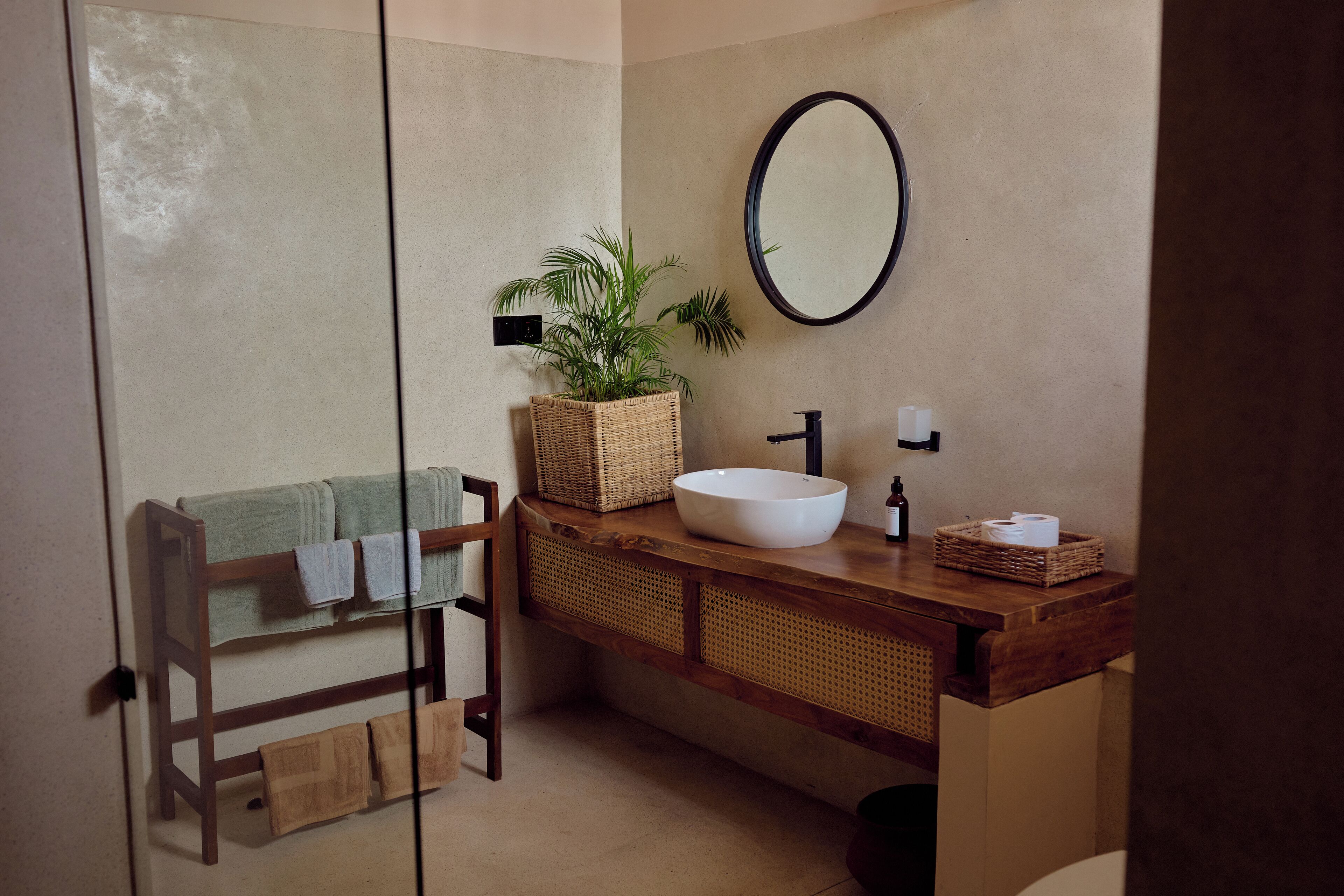 A bathroom with a wooden bench, a large mirror, a white sink, and a wicker basket with plants.