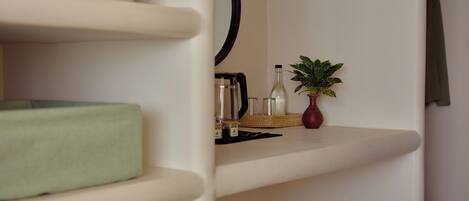 A modern, minimalist room with a green cushioned chair, a small table with a vase and a plant, and a mirror on the wall.