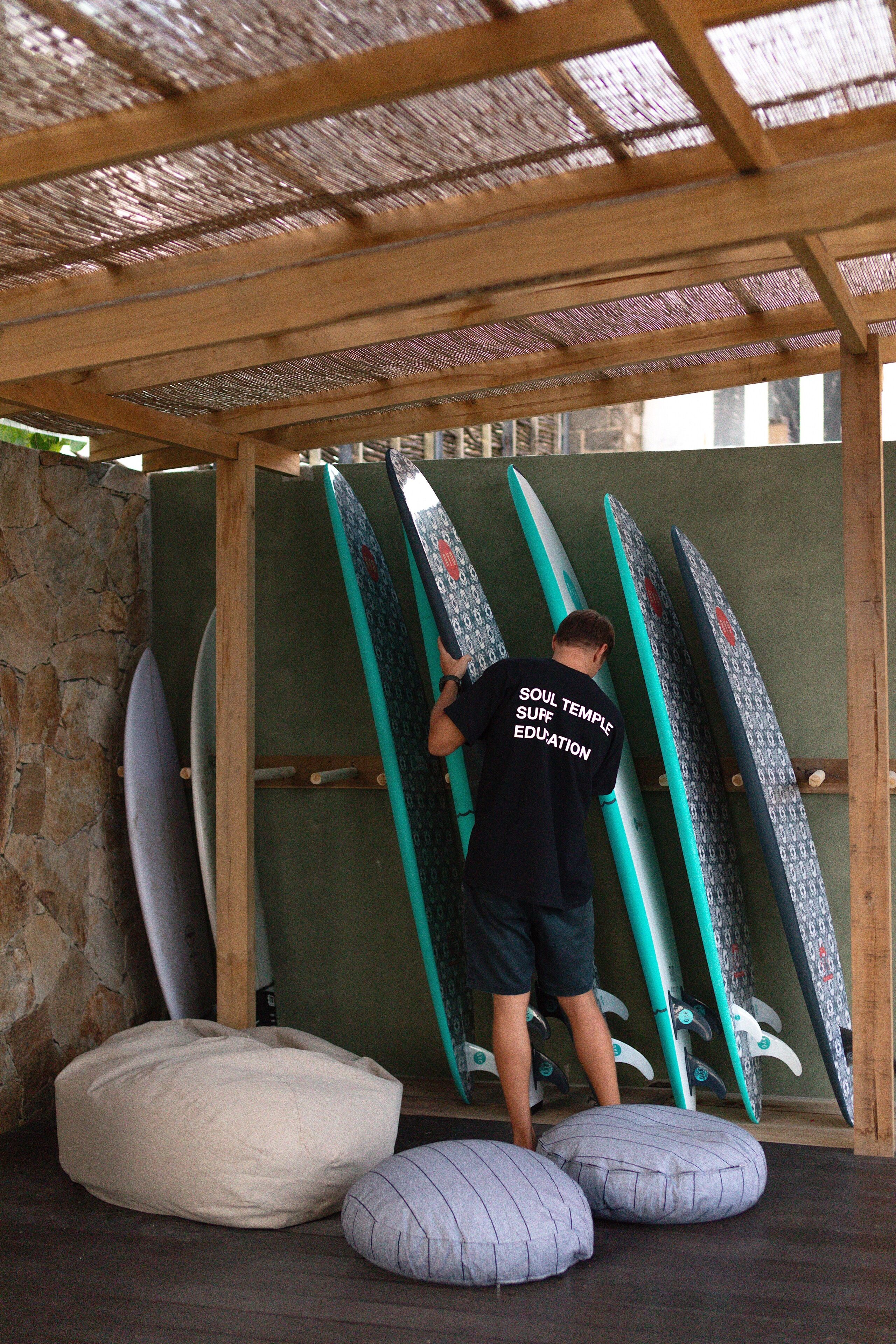 Una persona de pie en un espacio cubierto con tablas de surf apoyadas contra una pared.