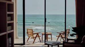 Una stanza con una grande finestra vista mare, due sedie di legno, un tavolino e una libreria.