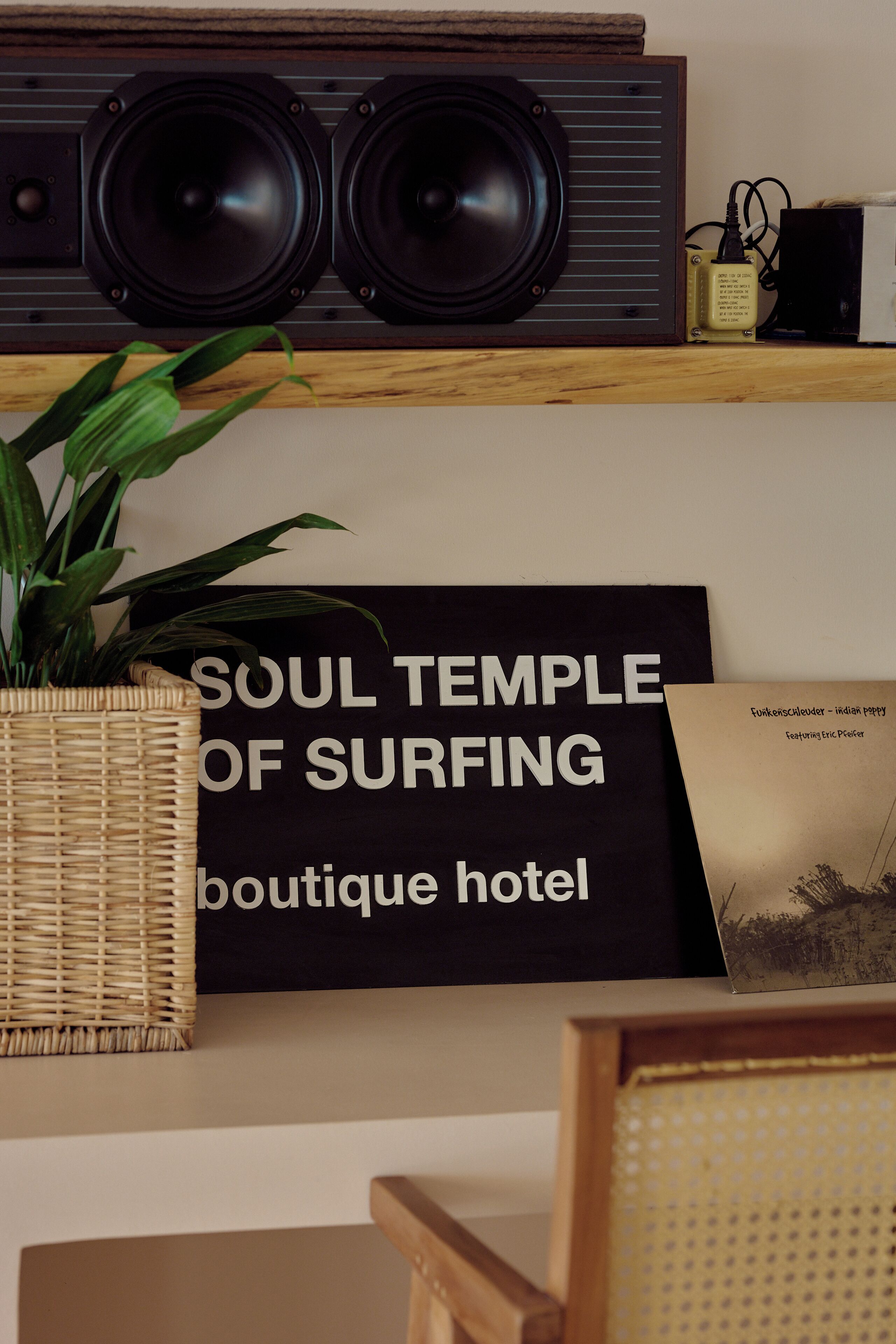 Una habitación con un estante de madera que sostiene un sistema de sonido grande, un letrero que dice "SOUL TEMPLE OF SURFING Boutique hotel", una foto enmarcada y una cesta de mimbre.
