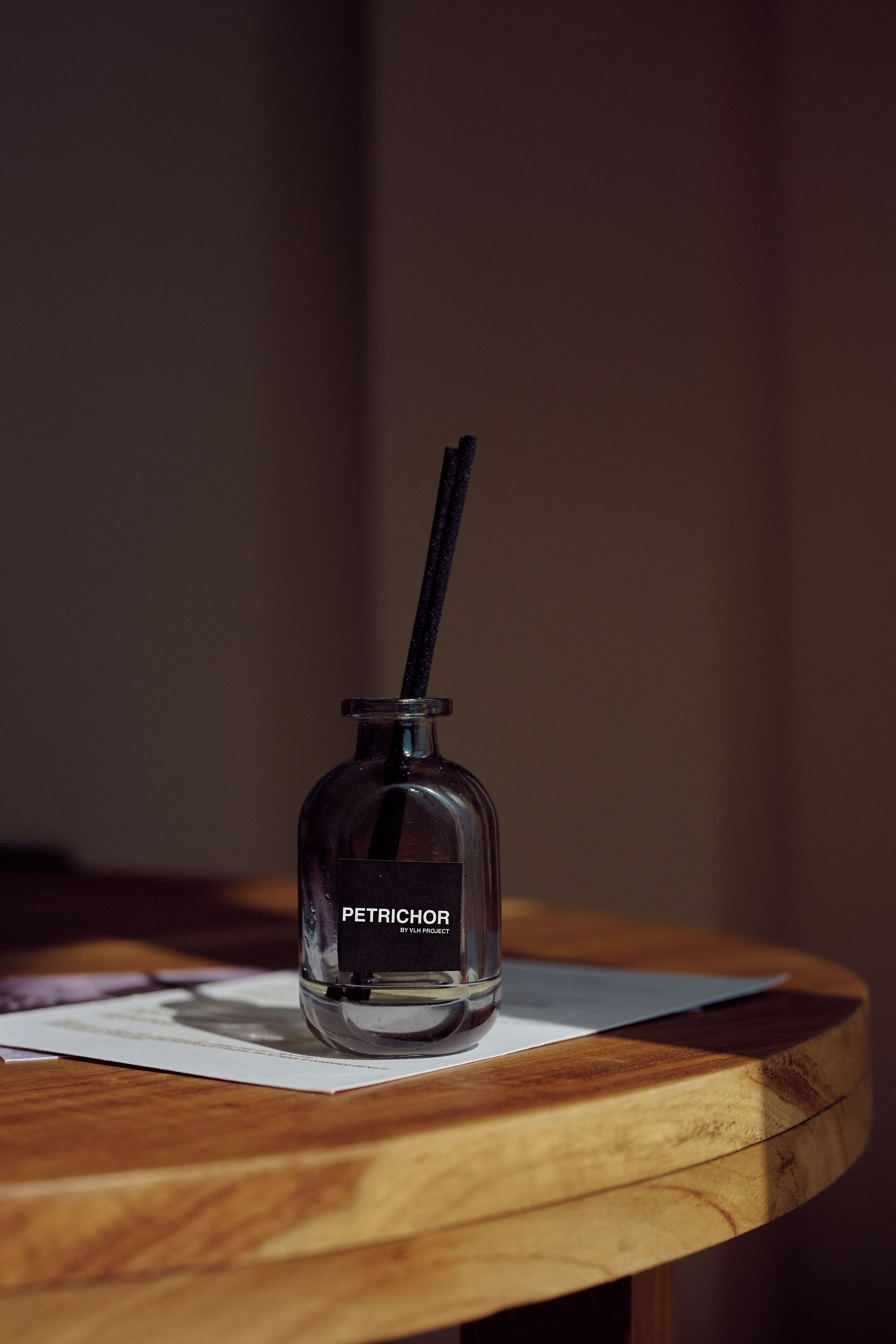Une petite bouteille en verre étiquetée « PÉTRICOR », avec une paille noire, posée sur une table en bois.