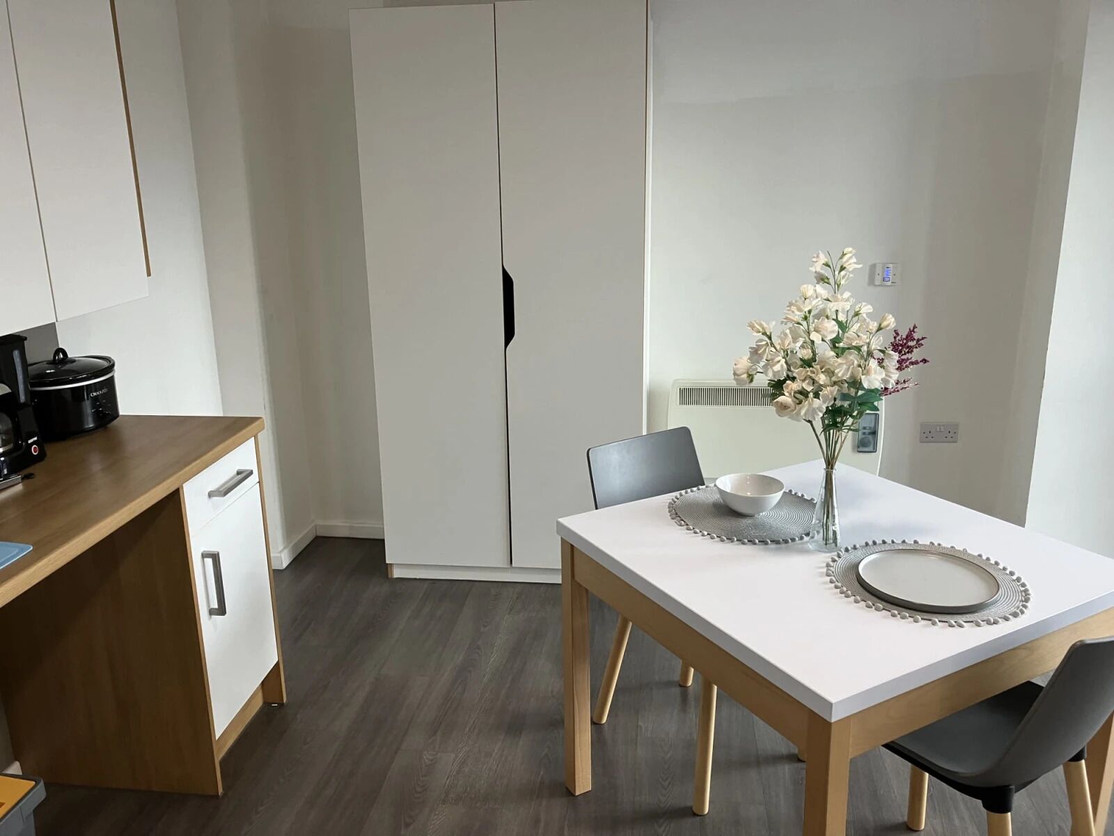 A modern kitchen with a wooden countertop, a coffee maker, and a white dining table with two chairs.