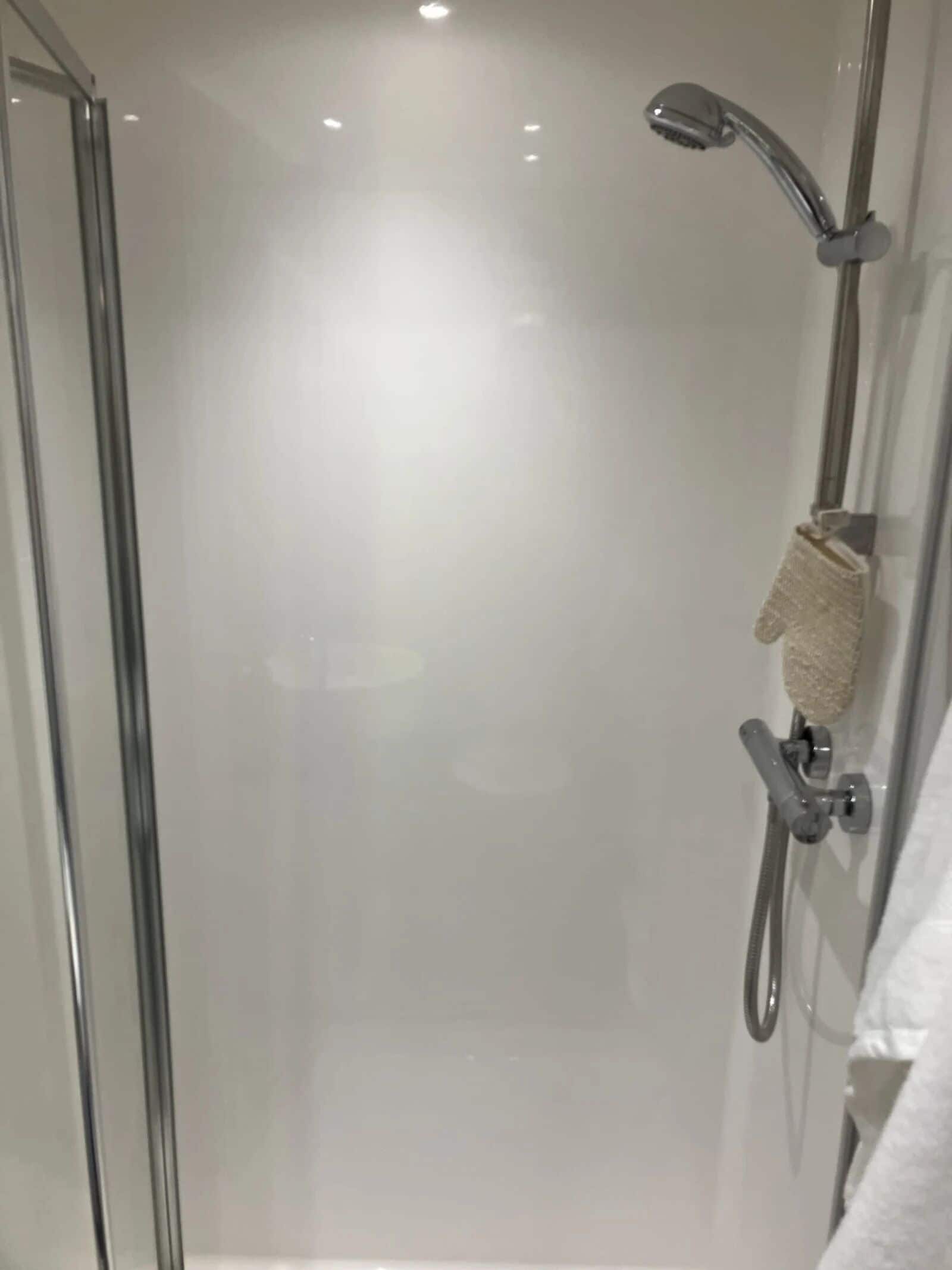 Un baño moderno con cabina de ducha de vidrio, un cabezal de ducha manual y un perchero para toallas.