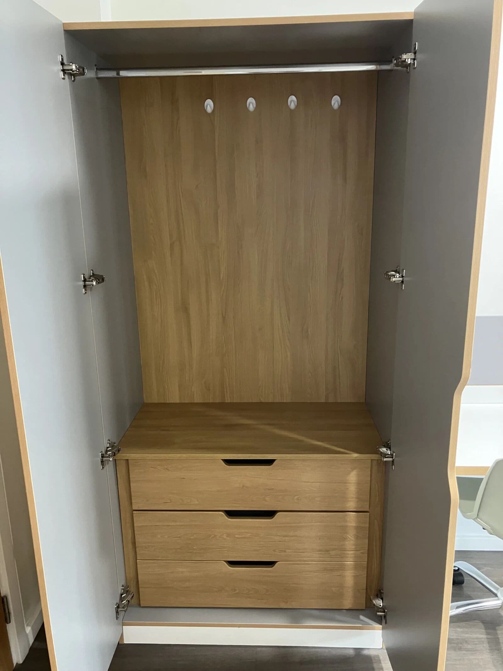 A wardrobe with a wooden finish, featuring a central hanging rod and two drawers.