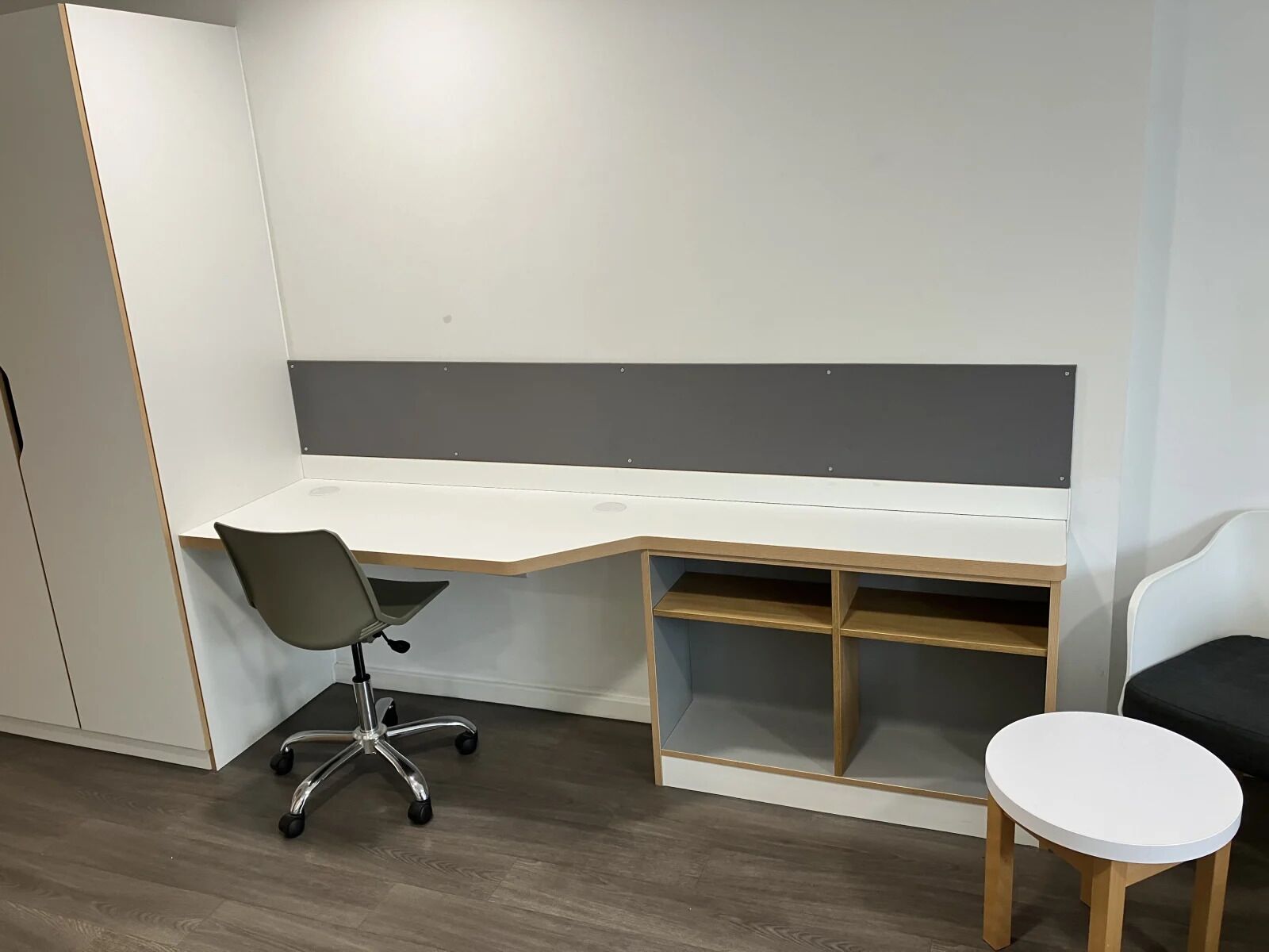 Un espacio de oficina moderno con un escritorio blanco, una silla de oficina gris y una pequeña mesa blanca.