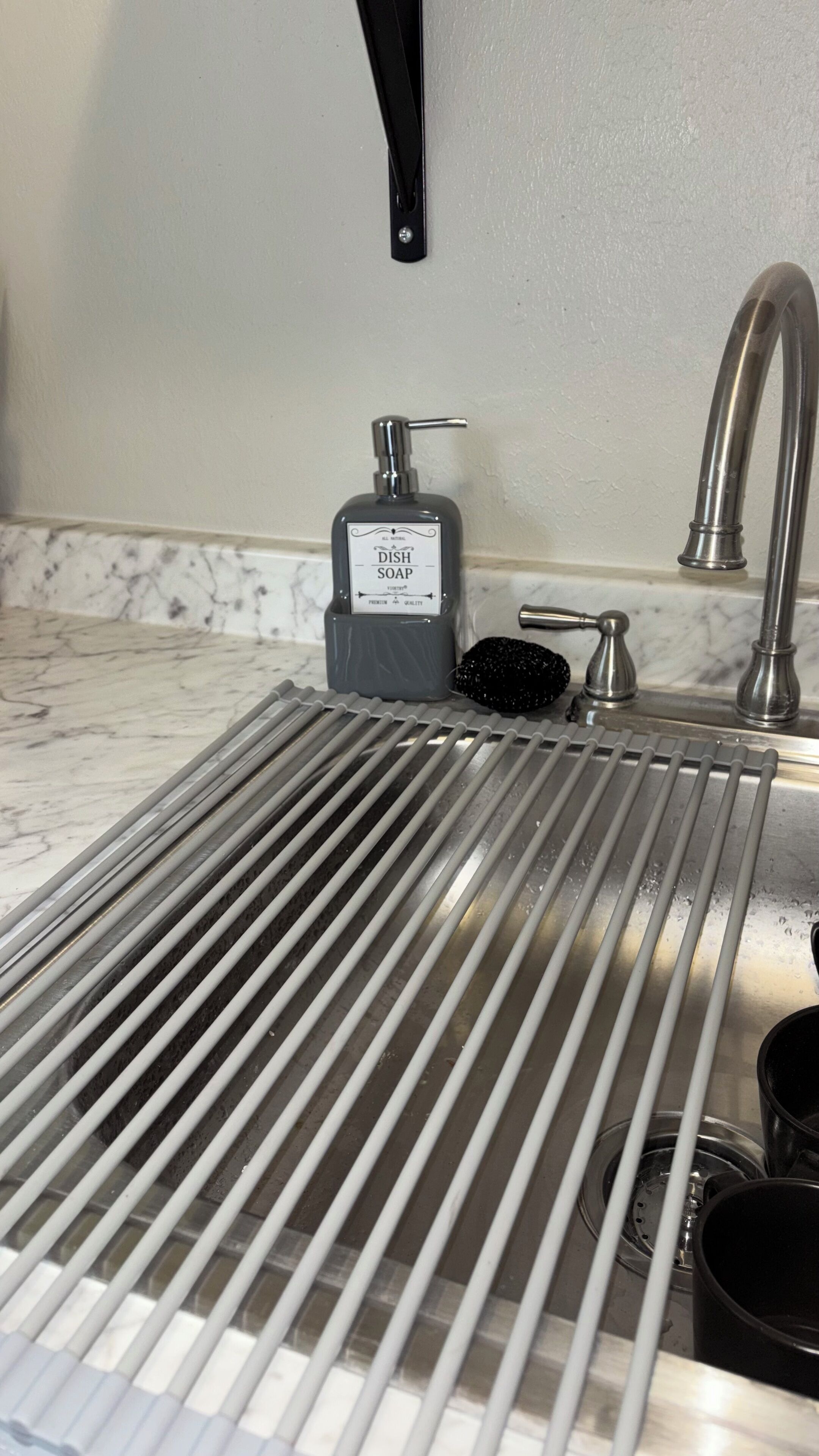 Un lavamanos de cocina con dispensador de jabón para trastes, un estropajo negro y un grifo.