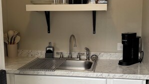 Una cocina con un lavamanos, una cafetera y una alacena con utensilios de cocina.