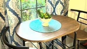 Un área de comedor con una mesa redonda, dos sillas y vistas al verdor a través de una ventana.