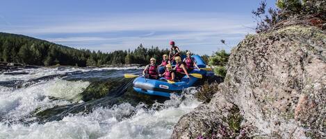 A group of people in a blue raft navigating a river with rapids.