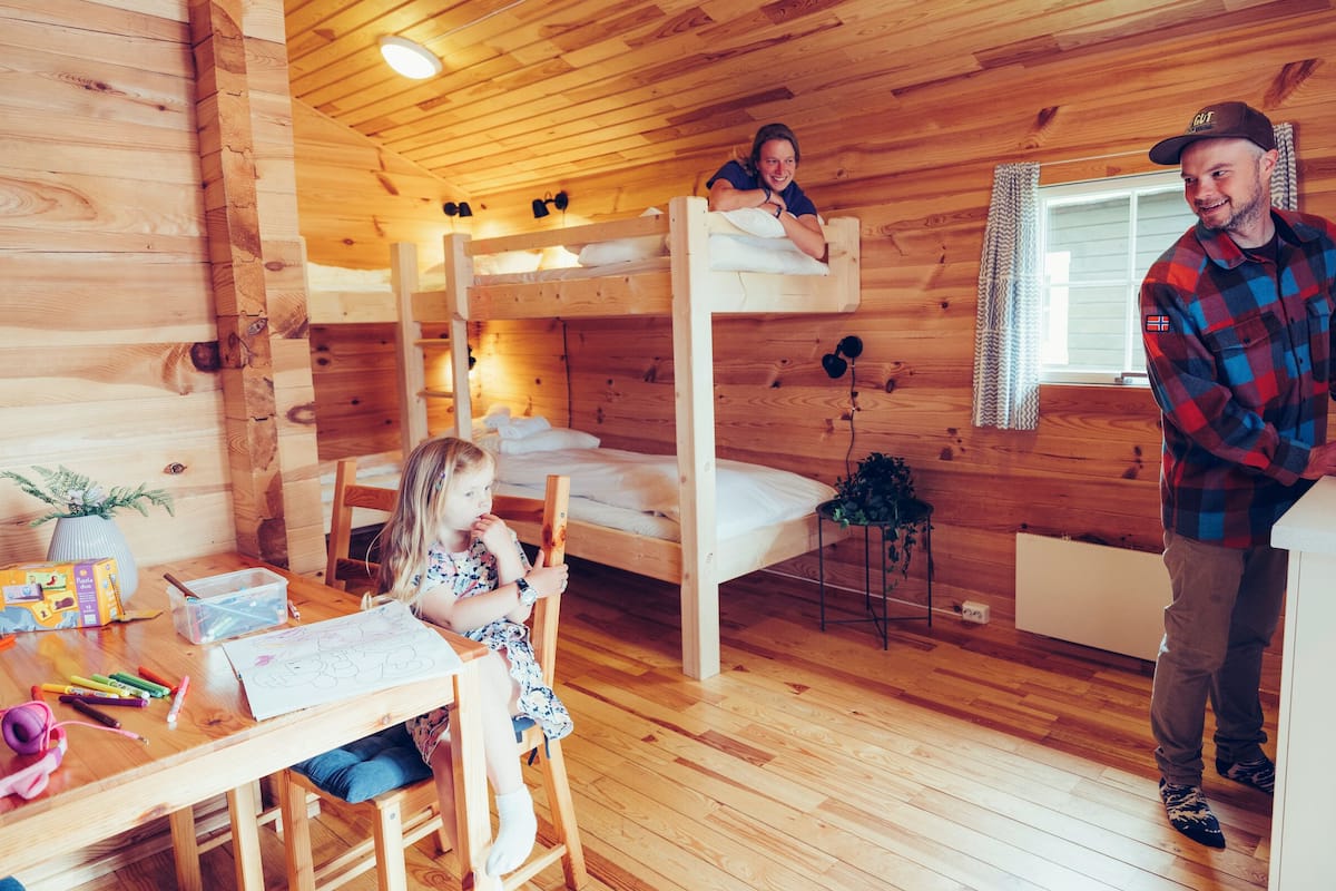 A cabin interior with bunk beds, a kitchen area, and a child at a desk with art supplies.