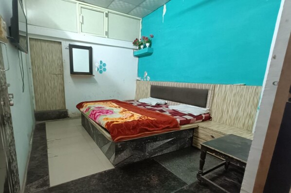 Een kleine slaapkamer met een bed, een tafeltje, een spiegel en een wandplank met bloemen.