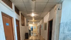 A long, narrow hallway with tiled floors, wooden doors, and a black mat at the end. - Trishala inn (Gwalior)
