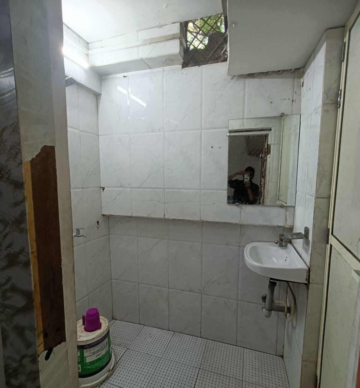 A bathroom with white tiled walls, a sink, and a mirror.