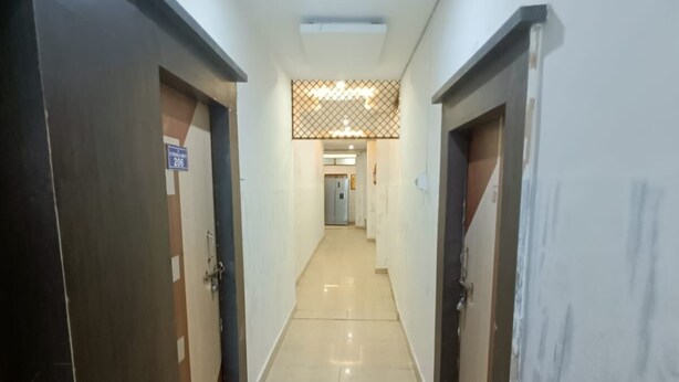 A hallway with two doors on either side, a tiled floor, and a ceiling light. - Trishala inn (Gwalior)