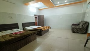 A hotel room with two beds, a chair, and a tiled floor. - Trishala inn (Gwalior)