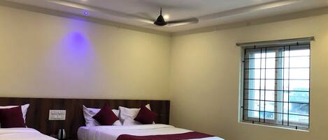 Ein Hotelzimmer mit zwei Betten, einem Deckenventilator, einer Klimaanlage, einem Fenster mit Gitterstäben und Blick nach draußen.