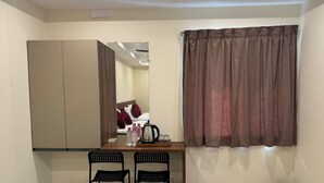 A small room with a bed, a table with chairs, a mirror, and a window with curtains. - Olive Nest Tirupati (Tirupati)