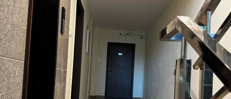 Ein Korridor mit Marmorboden, einer schwarzen Tür am Ende und einer Treppe auf der rechten Seite.