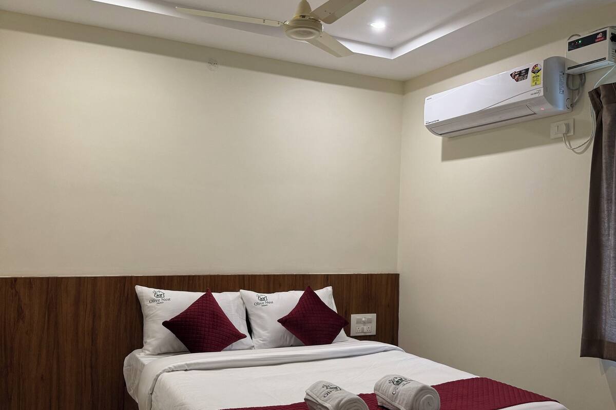 Ein Hotelzimmer mit einem hölzernen Kopfteil, einem Bett mit weißer und purpurroter Bettwäsche, einem Deckenventilator und einer Klimaanlage.