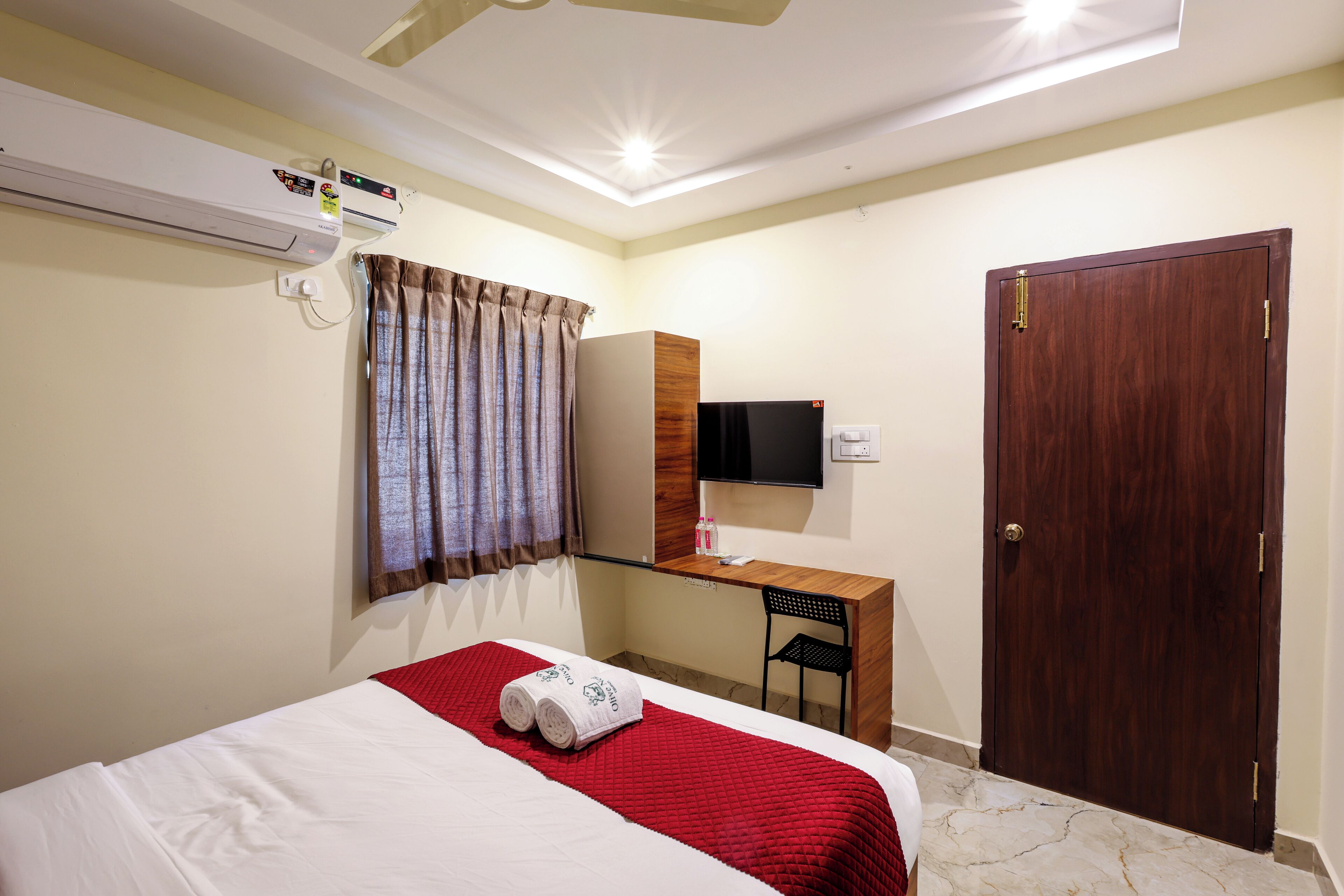 A hotel room with a bed, a desk, a television, and an air conditioning unit.