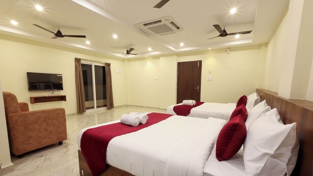 A hotel room with two beds, a TV, a sofa, and a sliding door to the balcony. - Olive Nest Tirupati (Tirupati)