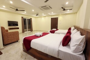 Habitación de hotel con dos camas, un televisor, un sofá y una puerta corrediza al balcón.