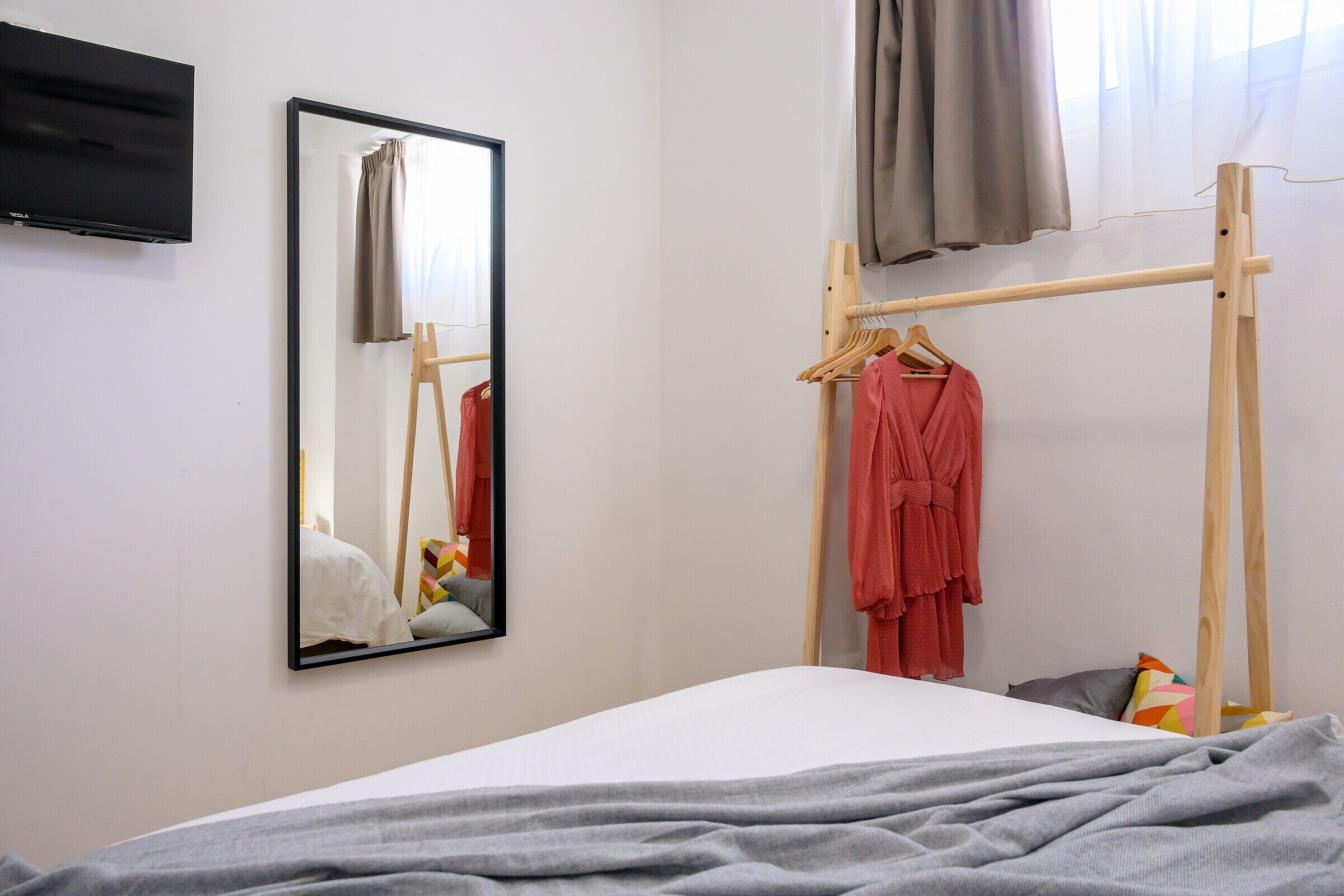 Una camera da letto con un letto, un armadio in legno, uno specchio e un televisore appeso al muro.