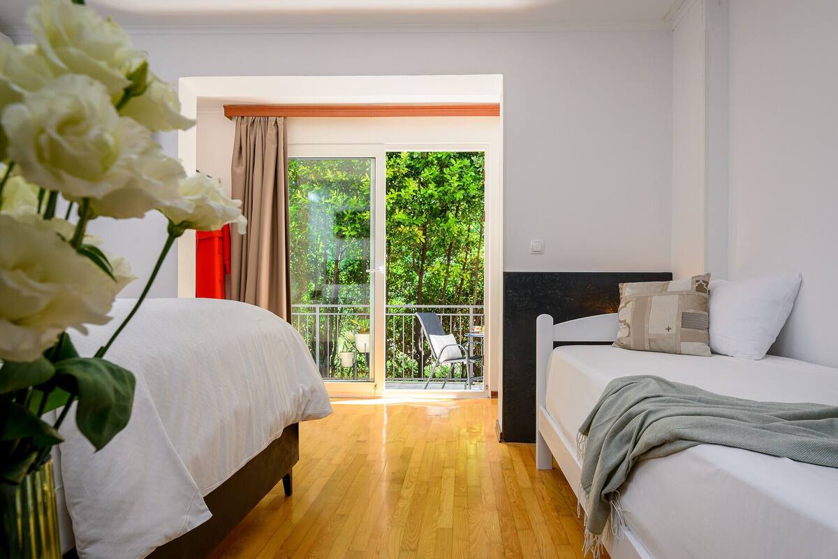 Un dormitorio con dos camas, un balcón con una silla y vistas a zonas verdes.