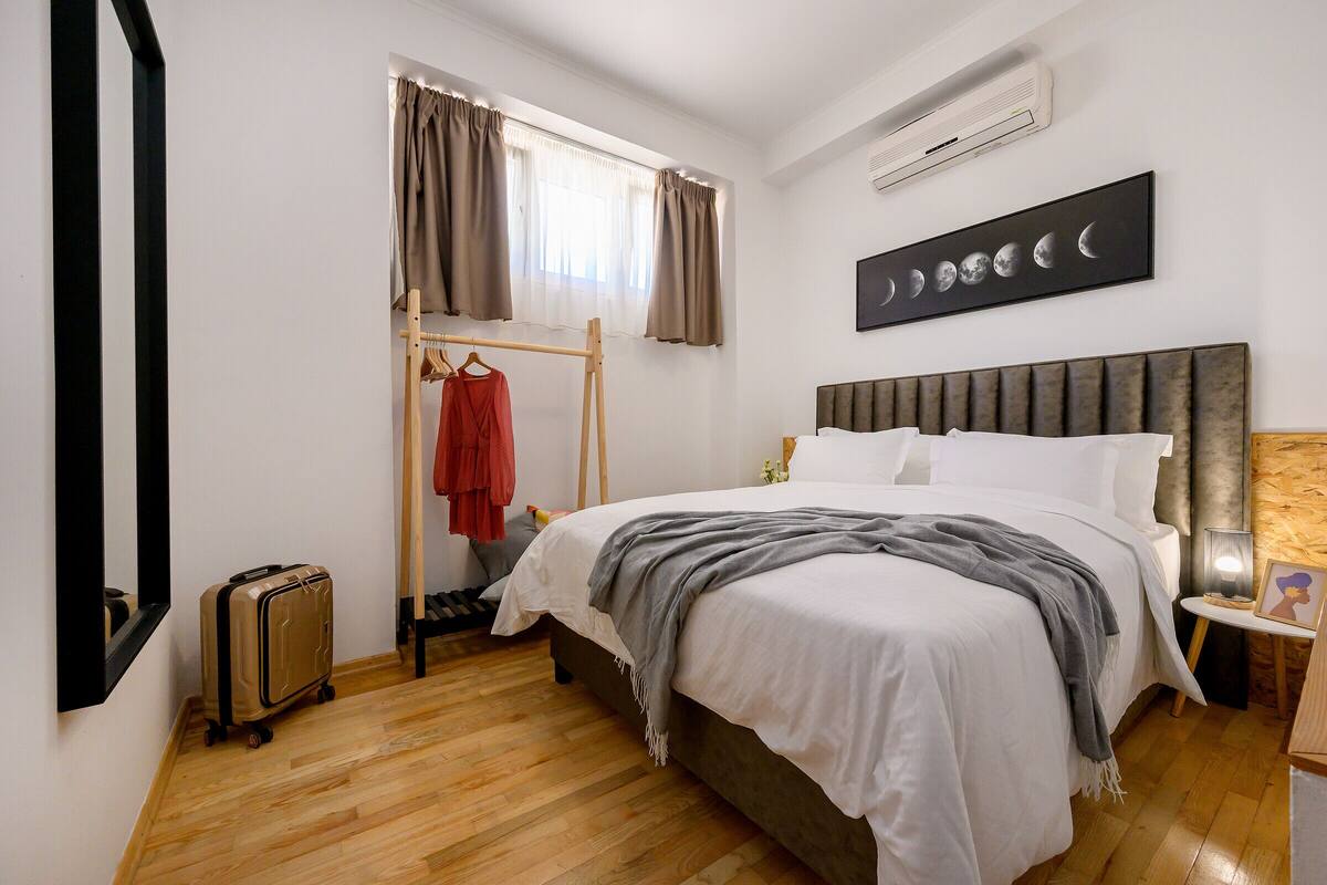 Un dormitorio con cama, perchero, maleta y aire acondicionado instalado en la pared.