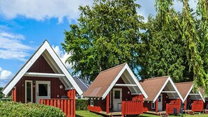 A row of red cabins with white trim, set in a grassy area with trees in the background. - 5 Person Holiday Park Home in Krusa (Krusaa)