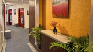 A reception area with a wooden reception desk, a painting on the wall, and potted plants. - C Suite - Lotus park (Bengaluru)