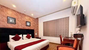 A hotel room with a brick wall, a large bed with red and white bedding, a wooden floor, a desk with a chair, and a large window. - C Suite - Lotus park (Bengaluru)