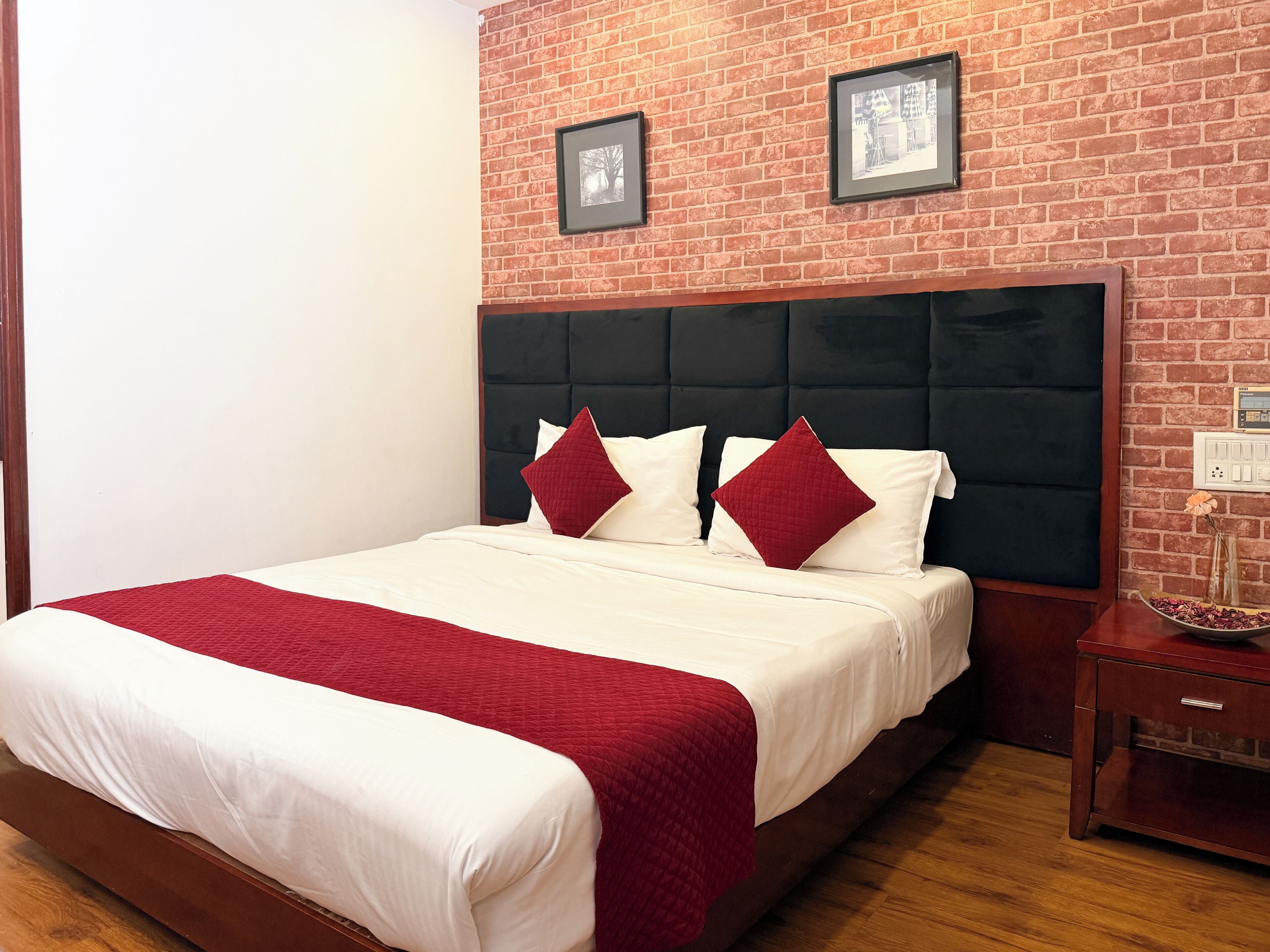 Habitación de hotel con pared de ladrillo, una cama grande con ropa de cama blanca y roja y una mesita de noche de madera.