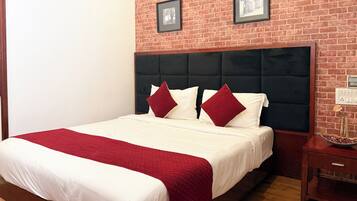 Habitación de hotel con pared de ladrillo, una cama grande con ropa de cama blanca y roja y una mesita de noche de madera.