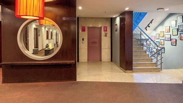 A hotel lobby with a round mirror, a red lamp, a staircase with framed pictures, and a 'No Drugs' sign. - C Suite - Lotus park (Bengaluru)