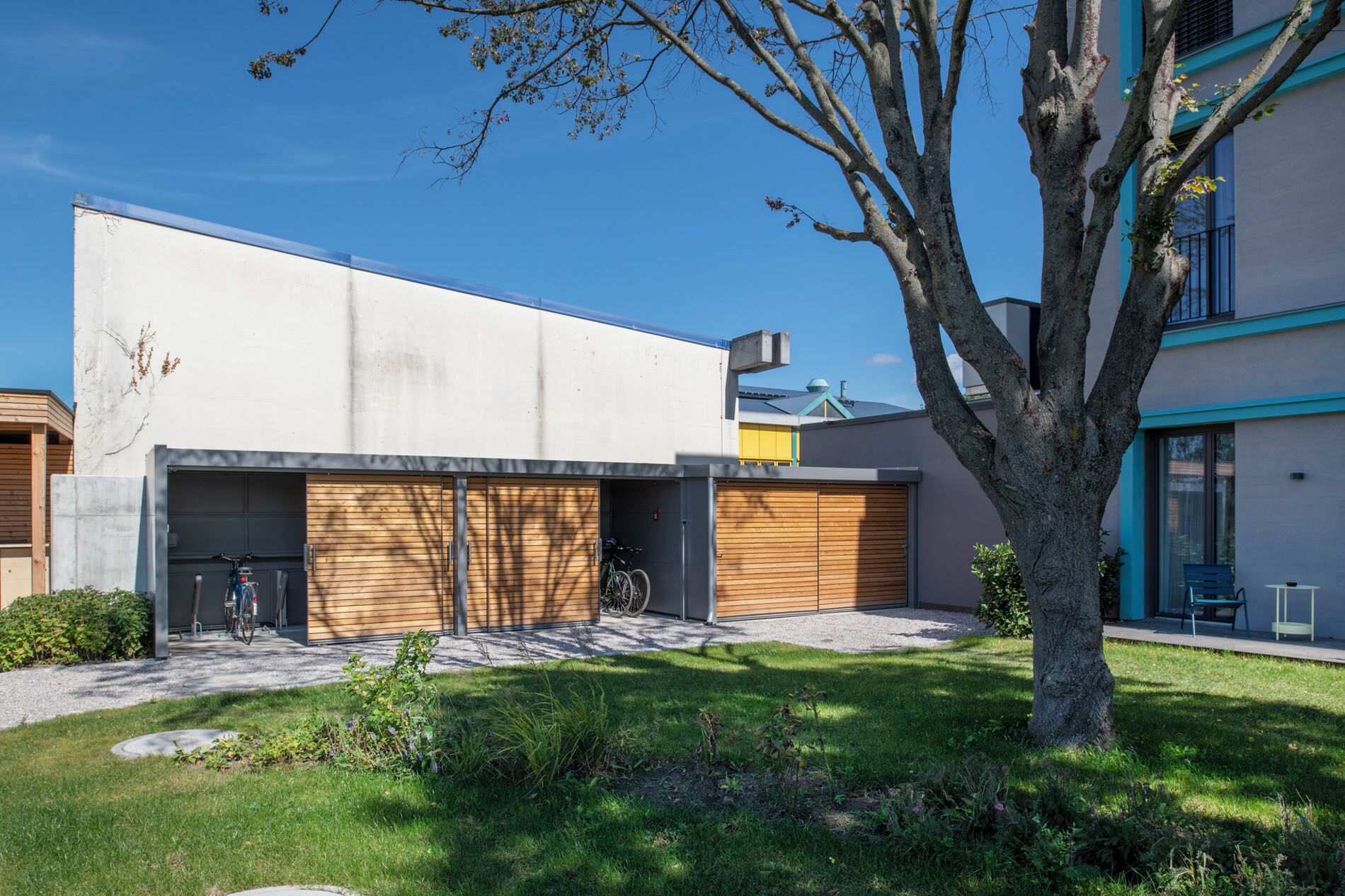 Un bâtiment moderne avec un garage, un vélo et un arbre dans la cour.