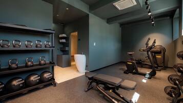 Une salle de sport équipée de kettlebells, d’haltères, d’un banc et d’autres appareils d’exercice.