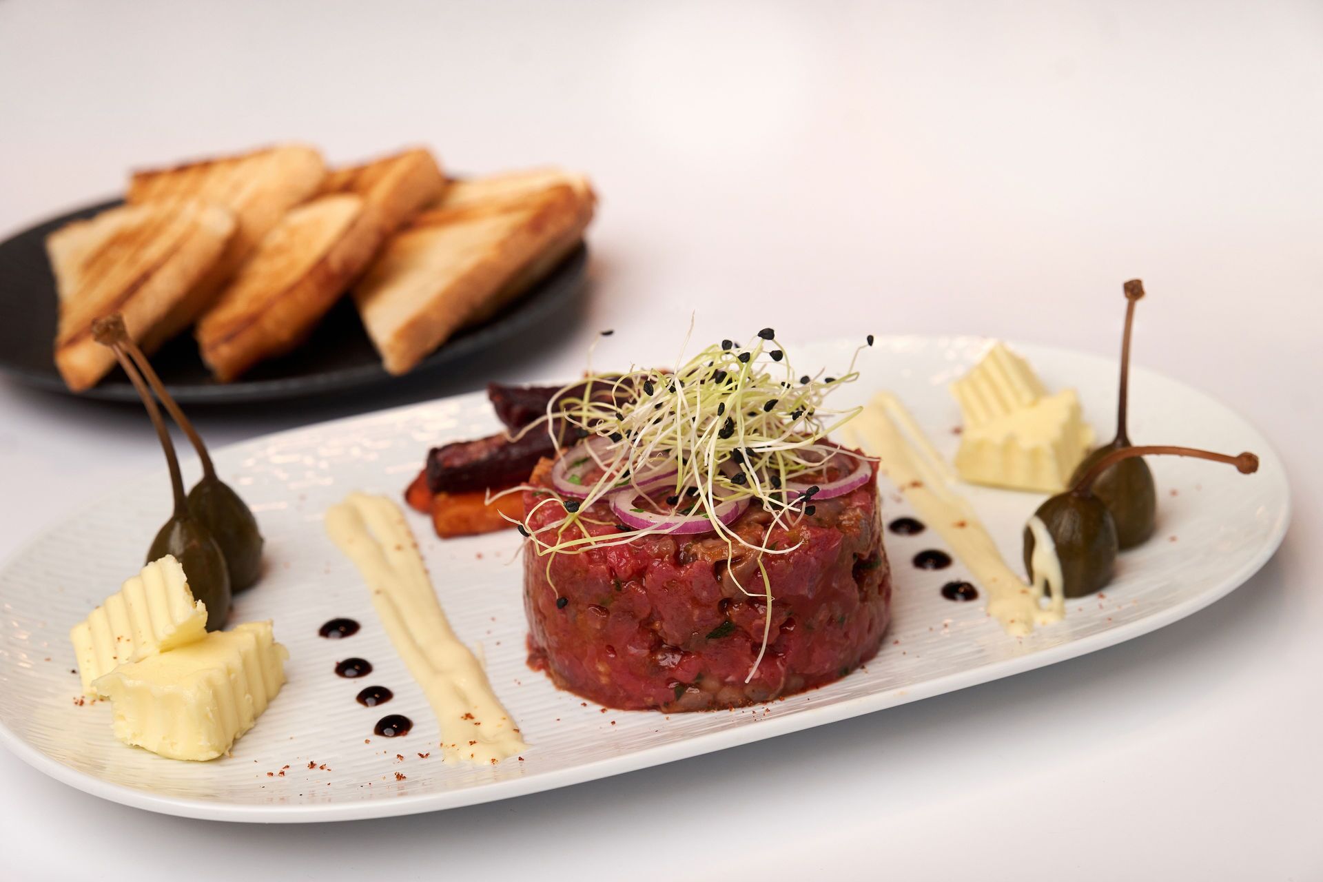A plate of steak tartare with garnishes and a side of bread.